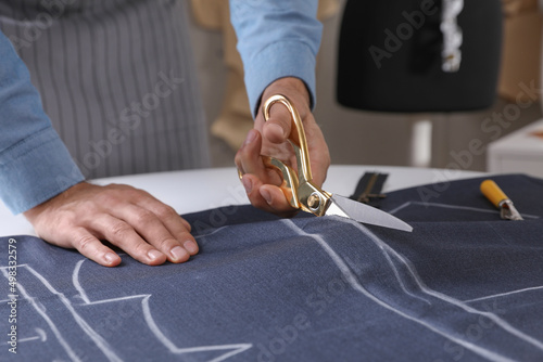 Tailor cutting fabric with scissors at table in atelier, closeup