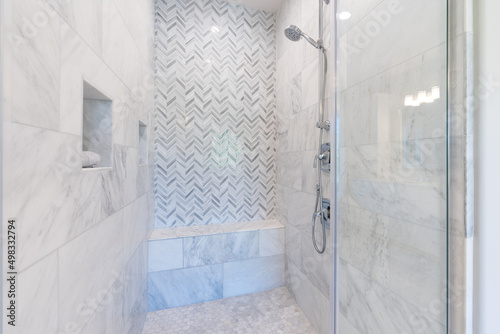 Walk-in shower with white and gray pattern tile, overhead rain shower, bench seating and chrome finishes.
