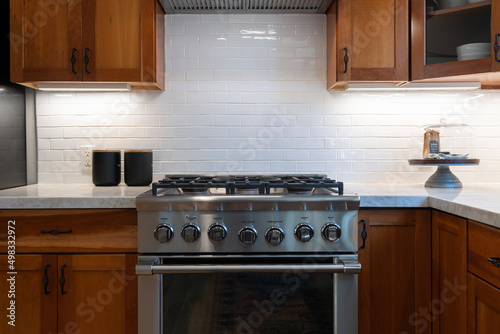 Modern stainless steel oven with wood cabinets and white tile backsplash.