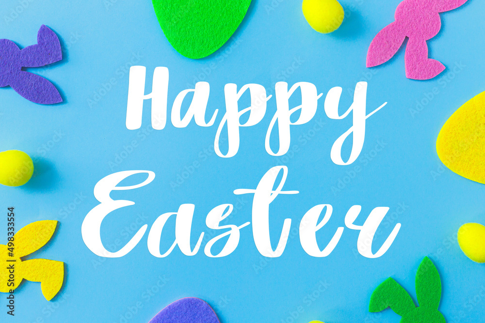 Happy Easter greeting card. Happy Easter text and colorful Easter bunnies and eggs frame on blue background flat lay. Seasons greeting card, handwritten lettering