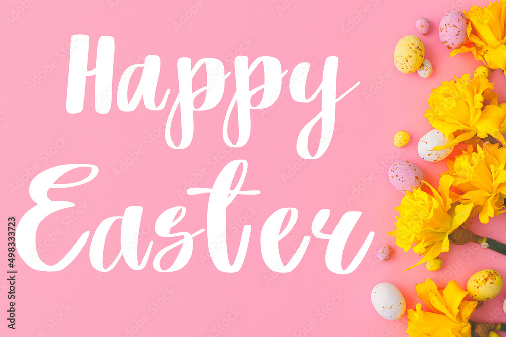 Happy Easter greeting card. Happy Easter text and colorful Easter chocolate eggs and daffodils flowers border on pink background flat lay. Seasons greeting card, handwritten lettering