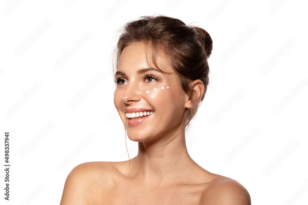 Smiling woman with moisturizing cream on the cheek. Beauty portrait with bare shoulders. Beauty and skincare concept. Isolated on white Smiling woman with moisturizing cream on the cheek. Beauty portrait with bare shoulders. Beauty and skincare concept. Isolated on white