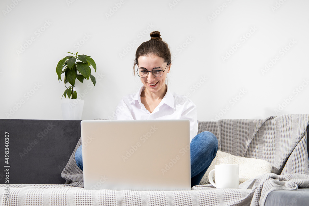 Smiling young woman in glasses using laptop sitting on sofa. Smiling young woman in glasses using laptop sitting on sofa.