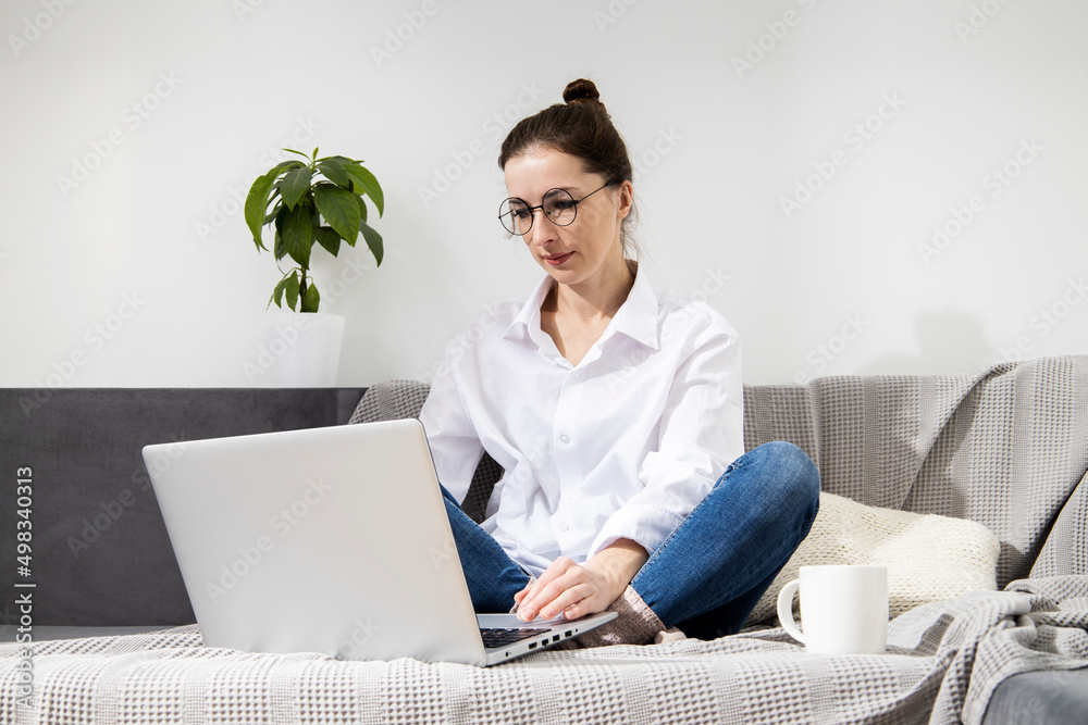 Young woman in glasses with laptop with coffee sitting on sofa. Young woman in glasses with laptop with coffee sitting on sofa.