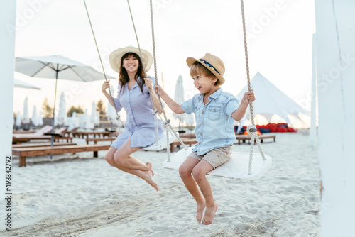 Mother and cute little son swinging on a big beautiful wooden swing on the beach at summer.