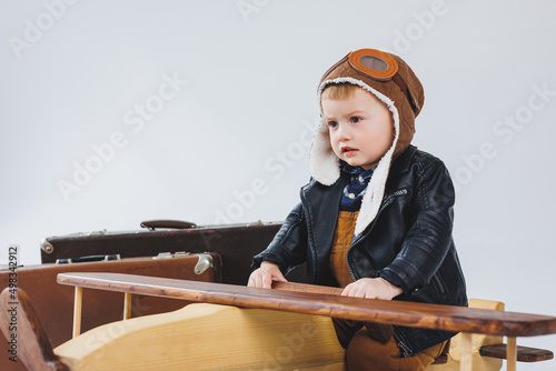 The boy is crying in a leather jacket and a pilot's hat, a wooden plane, brown suitcases. Children's wooden toys. Baby emotions