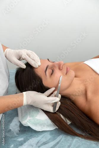 young woman in a beauty center performing a beauty treatment for the skin of the face with the dermaplaning technique photo