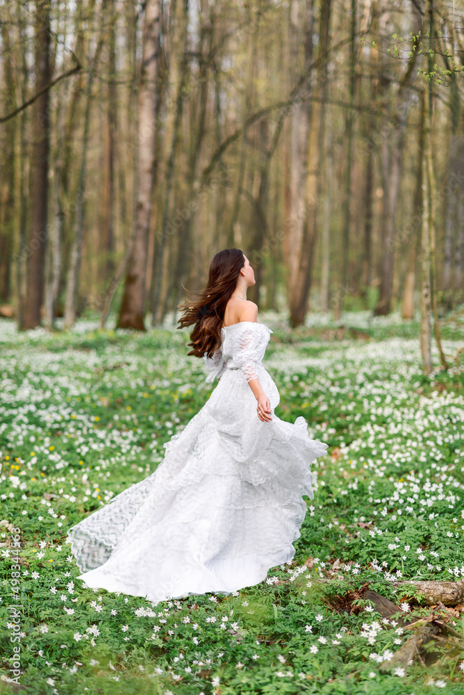 girl in a white long dress is spinning in a clearing with flowers. A young woman in the spring forest. girl in a white long dress is spinning in a clearing with flowers. A young woman in the spring forest.