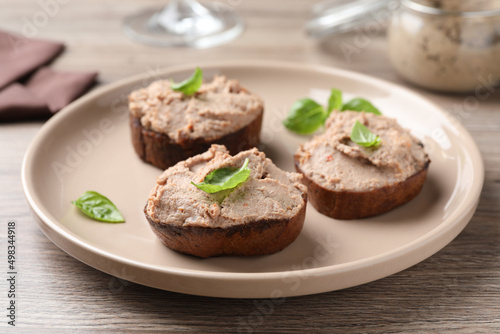 Slices of bread with delicious pate and basil on wooden table, closeup