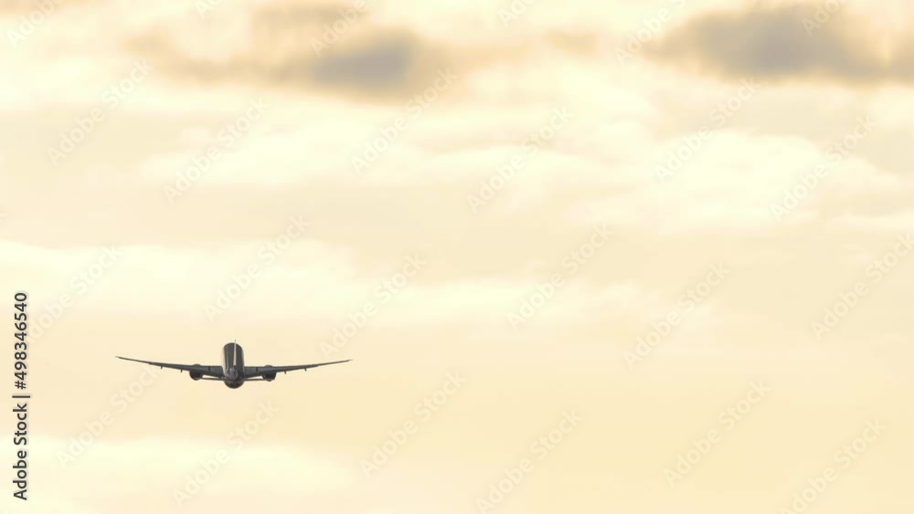 Airplane silhouette sunset sky. Long shot, a jet plane flies away gaining altitude. Golden cloudy sky at sunset or dawn Airplane silhouette sunset sky. Long shot, a jet plane flies away gaining altitude. Golden cloudy sky at sunset or dawn