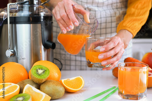 Young woman pours freshly fresh fruit juice into a glass. Making healthy fruit juices at home. Close-up. Selective focus.