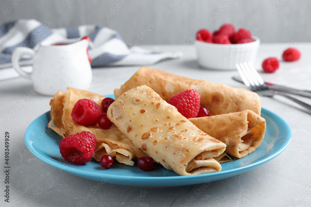 Delicious crepes served with berries on light grey table, closeup