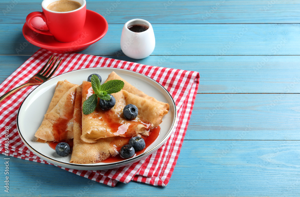Delicious crepes served with blueberries, mint, syrup and cup of coffee on blue wooden table. Space for text