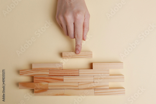 Woman finishing construction of wooden blocks on beige background, top view photo