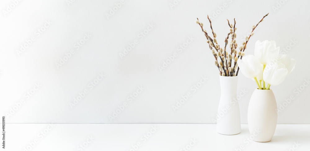 White spring tulips in a vase and willow branch on a white table. Mock up for displaying works