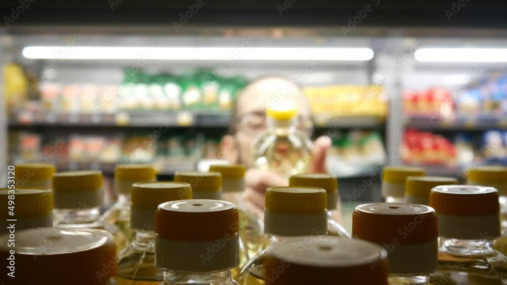Close-up of many sunflower oil bottles on a store shelf and a man takes one Close-up of many sunflower oil bottles on a store shelf and a man takes one