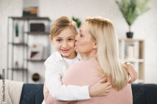 Close up smiling happy caucasian little boy embracing mum or babysitter, kissing on the cheek, holding, hugging each other, young woman hug small adopted daughter.