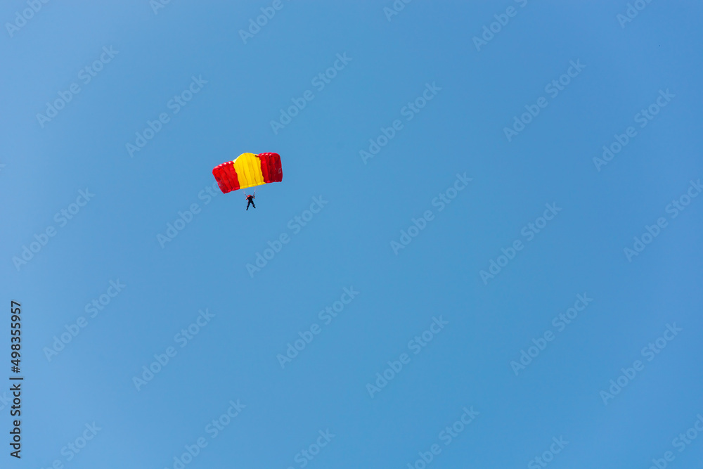 A red-yellow parachutist is planning against the blue sky. A red-yellow parachutist is planning against the blue sky.