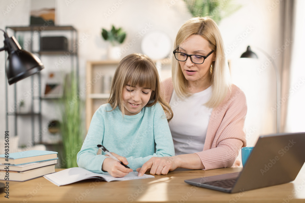 Caucasian tutor engaged with schoolgirl help complete tasks sitting at table at home. Concept of education kid development, european child homeschooling writing homework with stepmother concept Caucasian tutor engaged with schoolgirl help complete tasks sitting at table at home. Concept of education kid development, european child homeschooling writing homework with stepmother concept