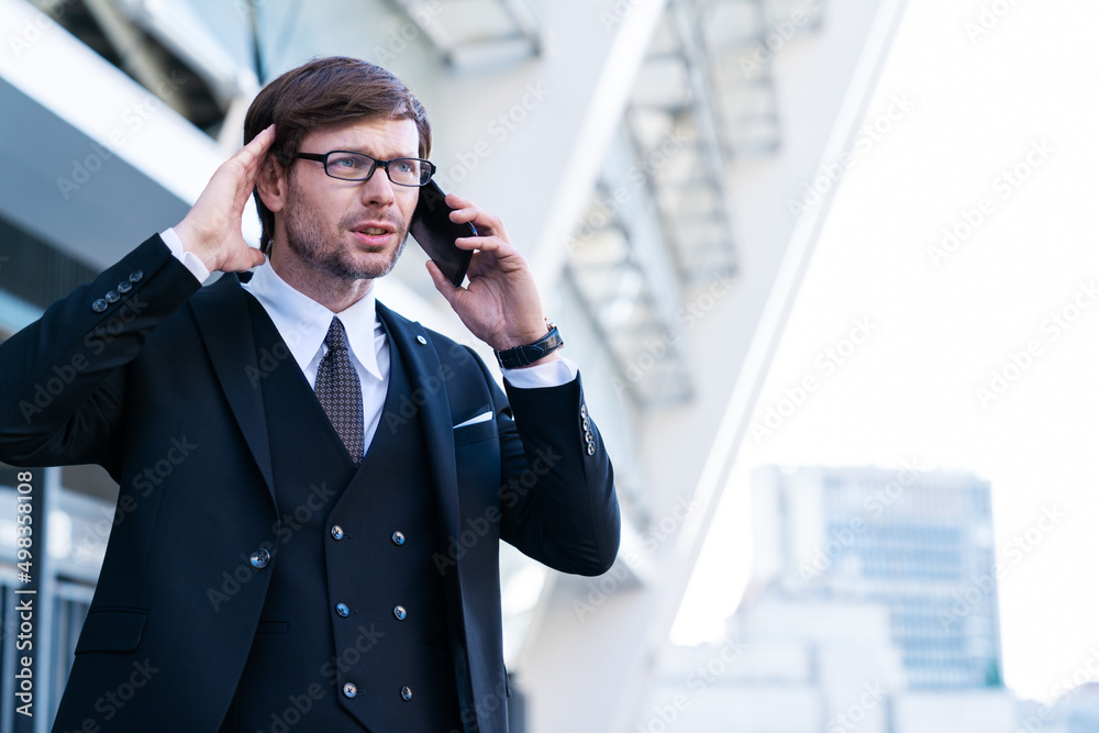 Portrait of stressed businessman speaks by phone with his head in hands in frustration. Overworked angry manger in big city business district. Upset man in suit with office building in background. Portrait of stressed businessman speaks by phone with his head in hands in frustration. Overworked angry manger in big city business district. Upset man in suit with office building in background.