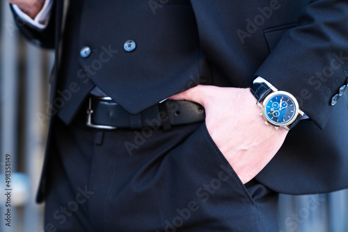 Closeup fashion image of luxury watch on wrist. Costume detail of a businessman. Hand in pocket closeup. Cheerful successful male wearing black jacket Stylish man go to work in elegant classic suit