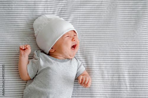 Close up of a crying newborn laying on a striped gray nappy. Hangry baby. Infantile colic. Baby care photo