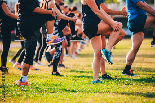 Fototapeta Naklejka Na Ścianę i Meble -  Group running warm up, Legs on beautiful green grass in warm light. Team training, stretching and core exercise