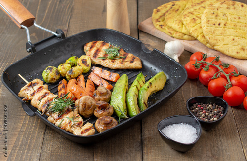 Grilled chicken breast and souvlaki with different vegetables in a pan.