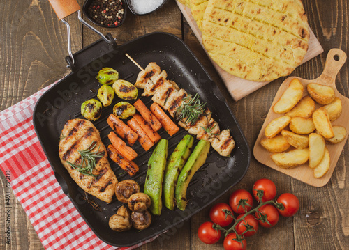 Grilled chicken steak and souvlaki in different variations with avocado, carrot, mushroom and brussels sprout on a teflon pan.