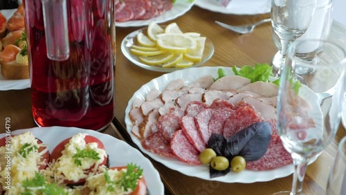 Festive table with large plates with variety of food, sausage, lemons, tomatoes, sandwiches with caviar on white dish photo