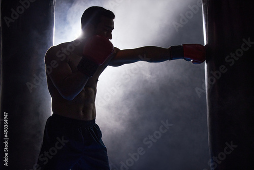 Working on his technique. Cropped shot of a silhouetted young male boxer working out on a punching bag in the gym.