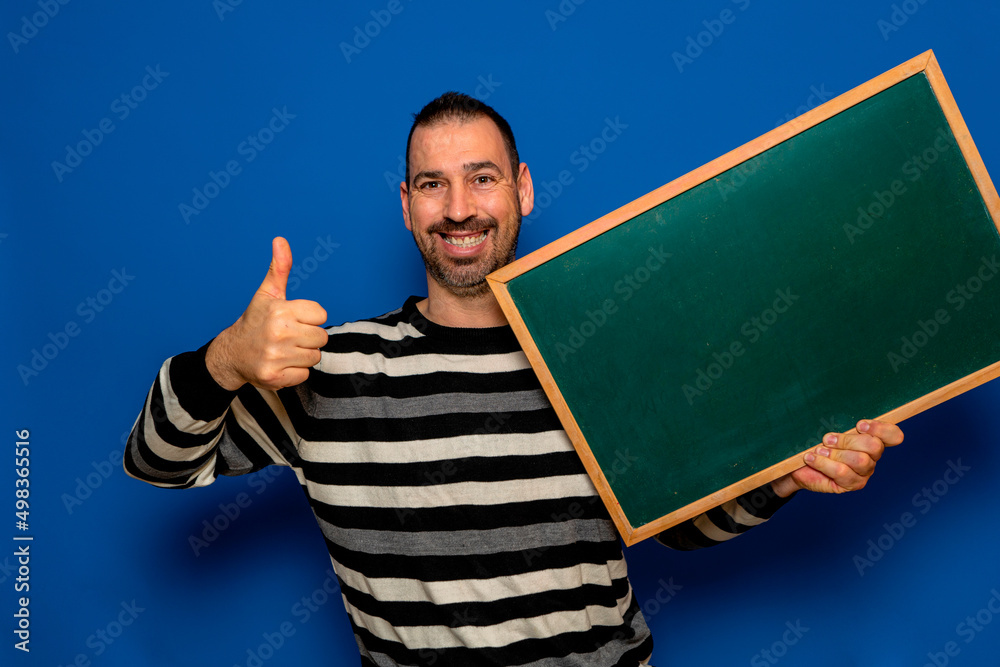 Happy bearded hispanic man showing, presenting and holding blank white board with thumb up isolated over blue background Happy bearded hispanic man showing, presenting and holding blank white board with thumb up isolated over blue background
