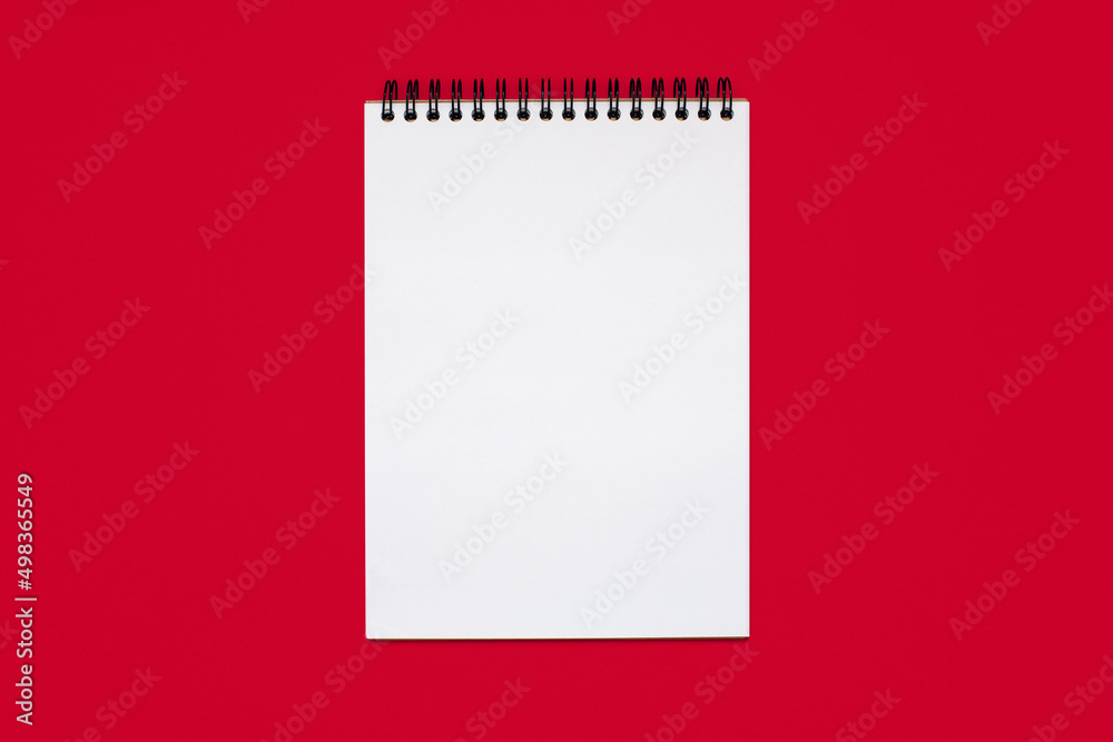 Notebook made of white paper with binding on a red background. Blank notepad with free space for text. Notebook in classic binding without notes, top view Notebook made of white paper with binding on a red background. Blank notepad with free space for text. Notebook in classic binding without notes, top view