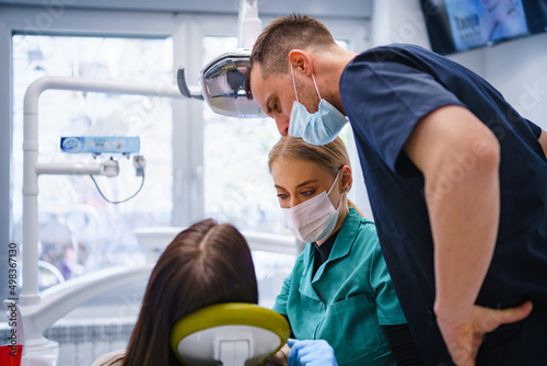 Two dentists examine and repair the patient's teeth. Three people in the dental office.