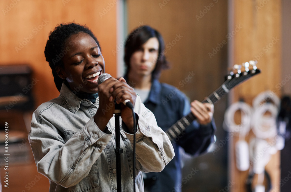 Waist up portrait of young black woman singing to microphone while rehearsing with band in professional recording studio