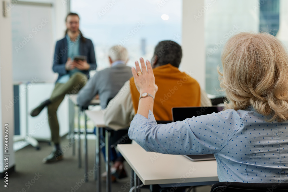 A senior woman is asking for an explanation in the computer course while sitting with elderly students in the classroom. A senior woman is asking for an explanation in the computer course while sitting with elderly students in the classroom.