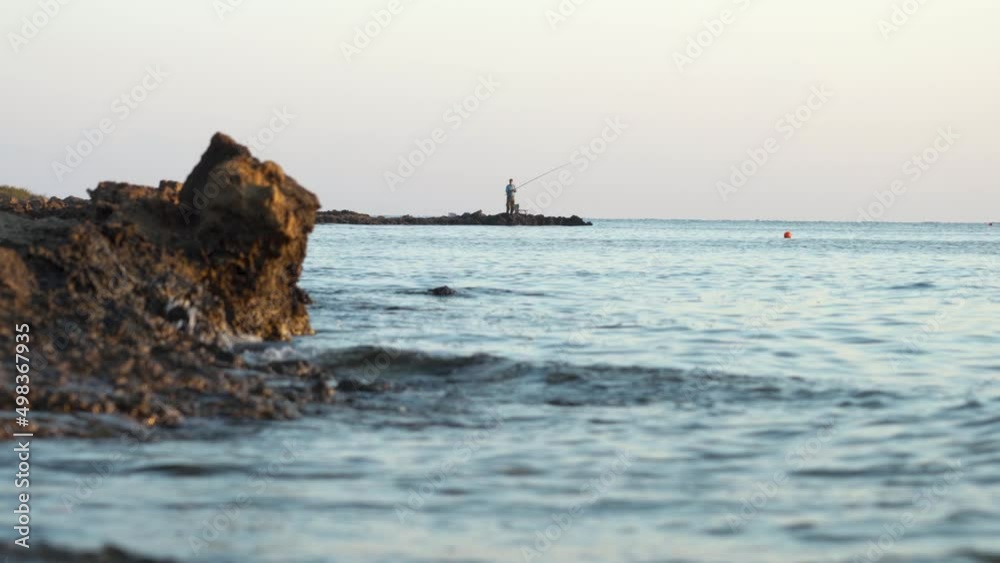 Silhouette of a fisherman fishing with a fishing rod in the early morning on the seashore Silhouette of a fisherman fishing with a fishing rod in the early morning on the seashore