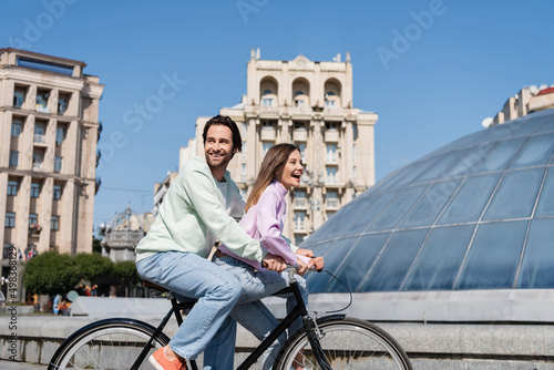 Cheerful couple cycling near building on urban street.