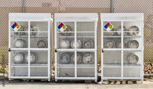 Quadro su tela Liquified Petroleum gas cylinders stored horizontally in a metal safety cage with NFPA warning signs on the closed doors, front view outside
