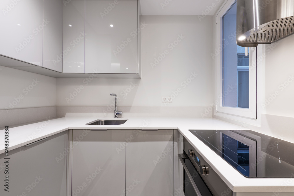 Kitchen with gloss gray wooden furniture combined with white stone countertop, ceramic hob and stainless steel extractor hood Kitchen with gloss gray wooden furniture combined with white stone countertop, ceramic hob and stainless steel extractor hood