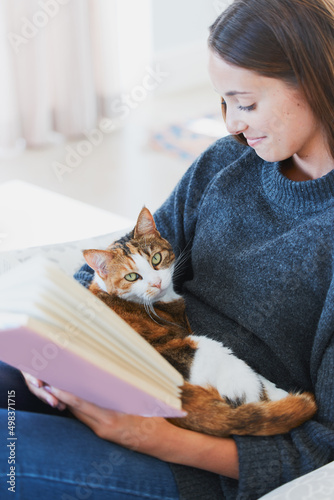 Happiness is a fluffy cat and a great book. Shot of a young woman reading a book with a cat on her lap at home.