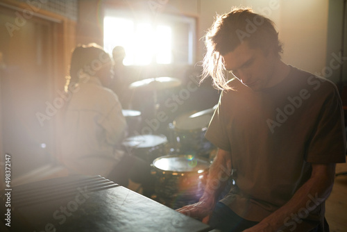 Moody portrait of long haired young man playing music rehearsing with band in dim sunlight, copy space photo