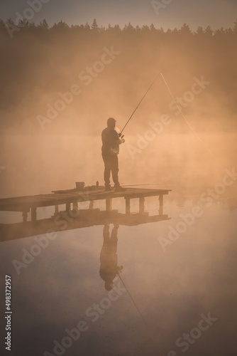 Obraz na płótnie Beautiful morning scene by the lake. Silhouette of a man fishing on a wooden pier in the light of the rising sun. w salonie
