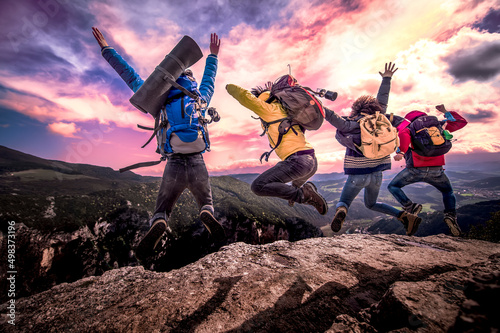 Fotobehang Happy friends hikers with open arms jumping on the top of mountain and enjoys sunset - Tourists, people, expedition, freedom, success and sport concept