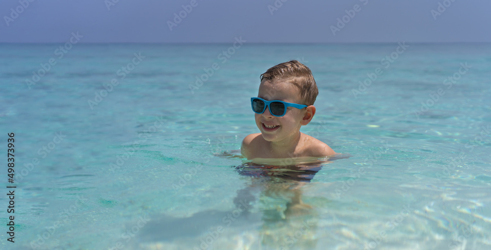 Happy child in sunglasses swims in the Indian Ocean in Maldives