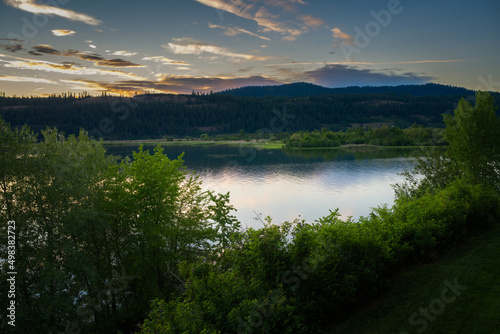 2022-04-11 COEUR D'ALENE RIVER NEAR HARRISON IDAHO WITH A NICE REFLECTION AND BRIGHT GREEN TREES IN THE FOREGROUND WITH A MOUNTAIN RANGE AND NICE SKY AT DUSK