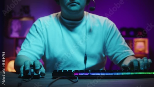Gamer playing computer game, streamer wearing headphones. Young man playing video games using backlight keyboard. Programmer or hacker working in networks, cyberspace. photo