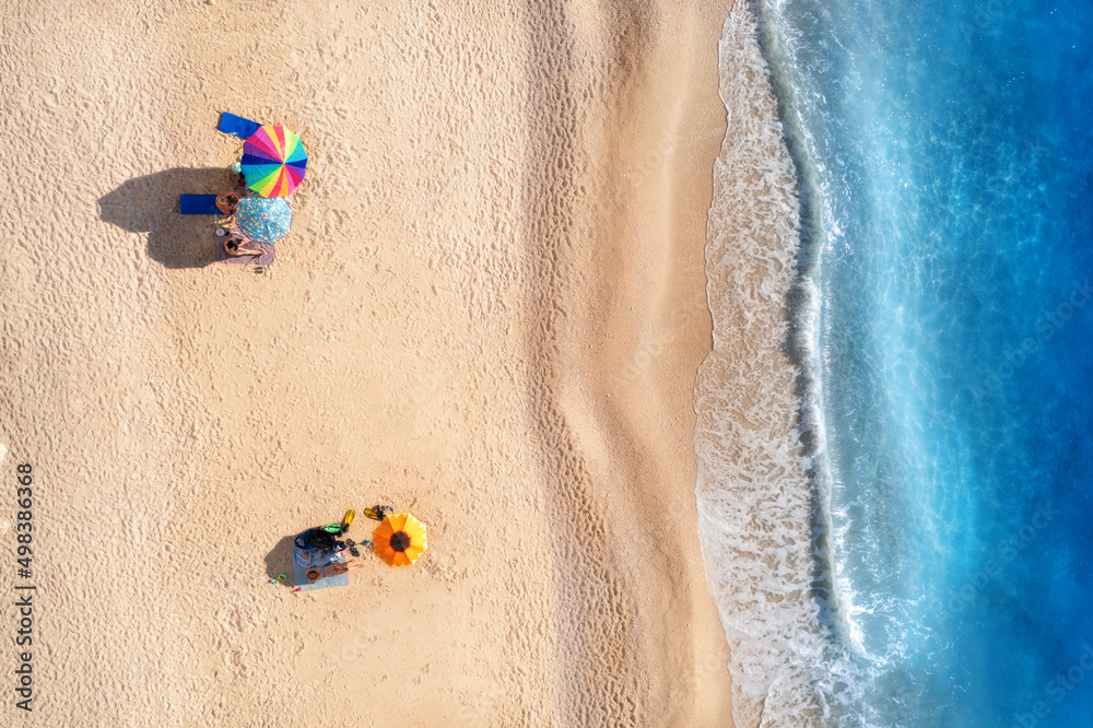 Aerial view of blue sea, waves, sandy beach and umbrellas with lying people at sunset in summer. Tropical landscape with clear turquoise water. Top view from drone. Lefkada island, Greece. Travel