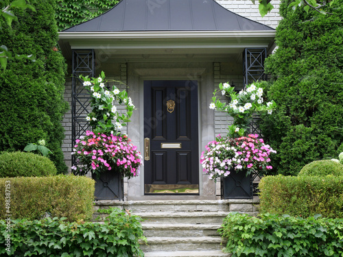 Elegant black and brass front door surrounded by flowers and bushes © Spiroview Inc.