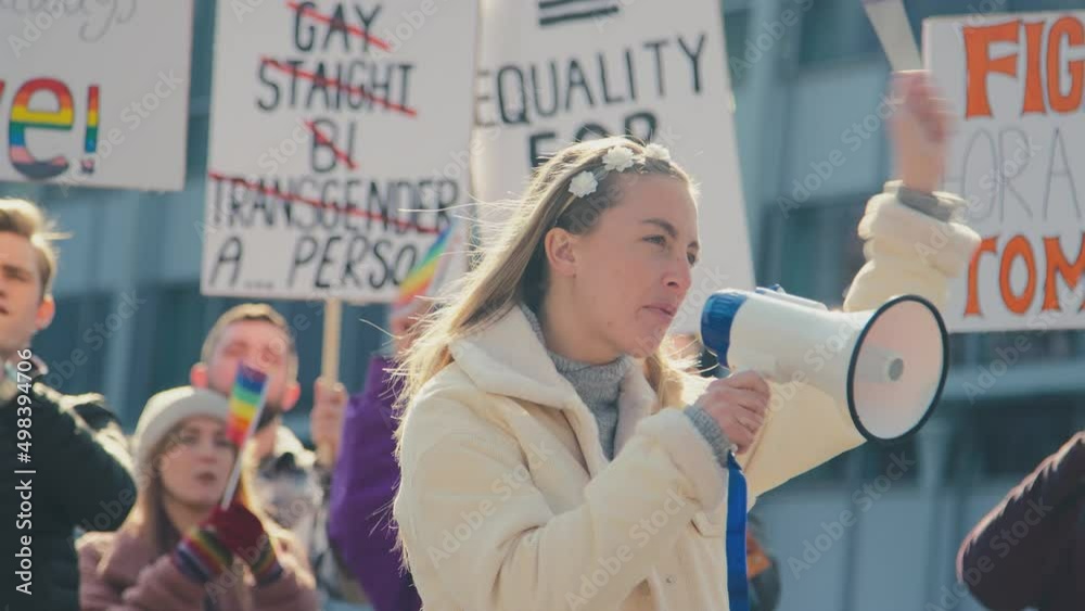 Group of protestors with megaphone holding placards and waving flags on demonstration march to promote gender equality- shot in slow motion